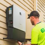 Jak współpracuje fotowoltaika z systemami smart home i zdalnym sterowaniem światłem Technik montujący falownik fotowoltaiczny na zewnątrz domu