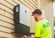Jak współpracuje fotowoltaika z systemami smart home i zdalnym sterowaniem światłem Technik montujący falownik fotowoltaiczny na zewnątrz domu