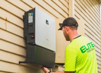 Jak współpracuje fotowoltaika z systemami smart home i zdalnym sterowaniem światłem Technik montujący falownik fotowoltaiczny na zewnątrz domu